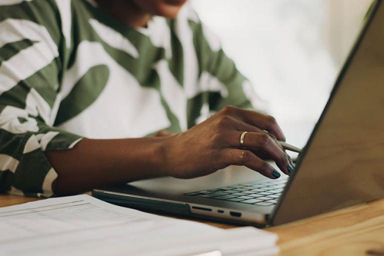 a woman using a laptop with a notebook to one side